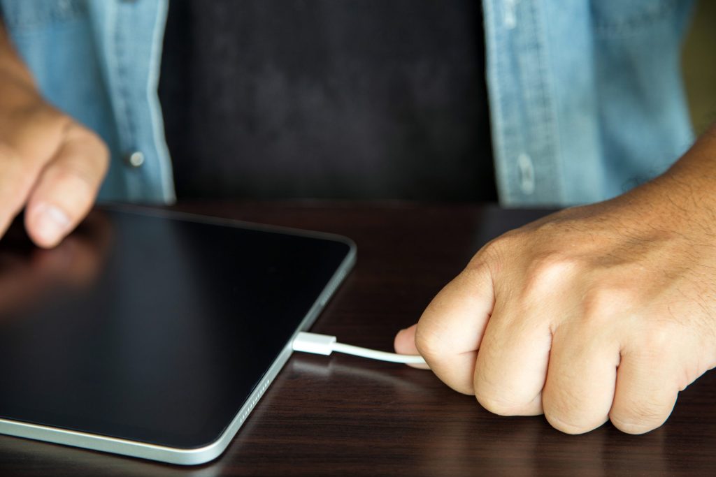 mans hand unplugging tablet charger wooden table wrong way
