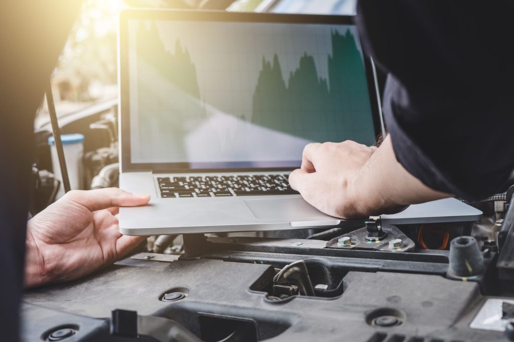 midsection mechanic repairing car while using laptop